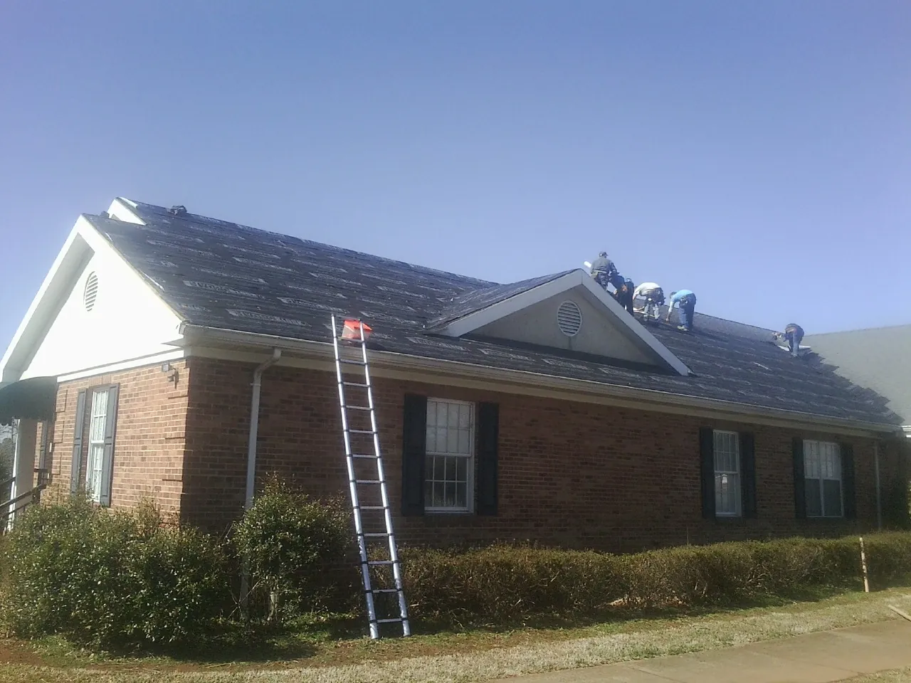 Crew tearing shingles off a brick ranch roof with a ladder set — Emergency Roof Repair work by our crew in Nescopeck