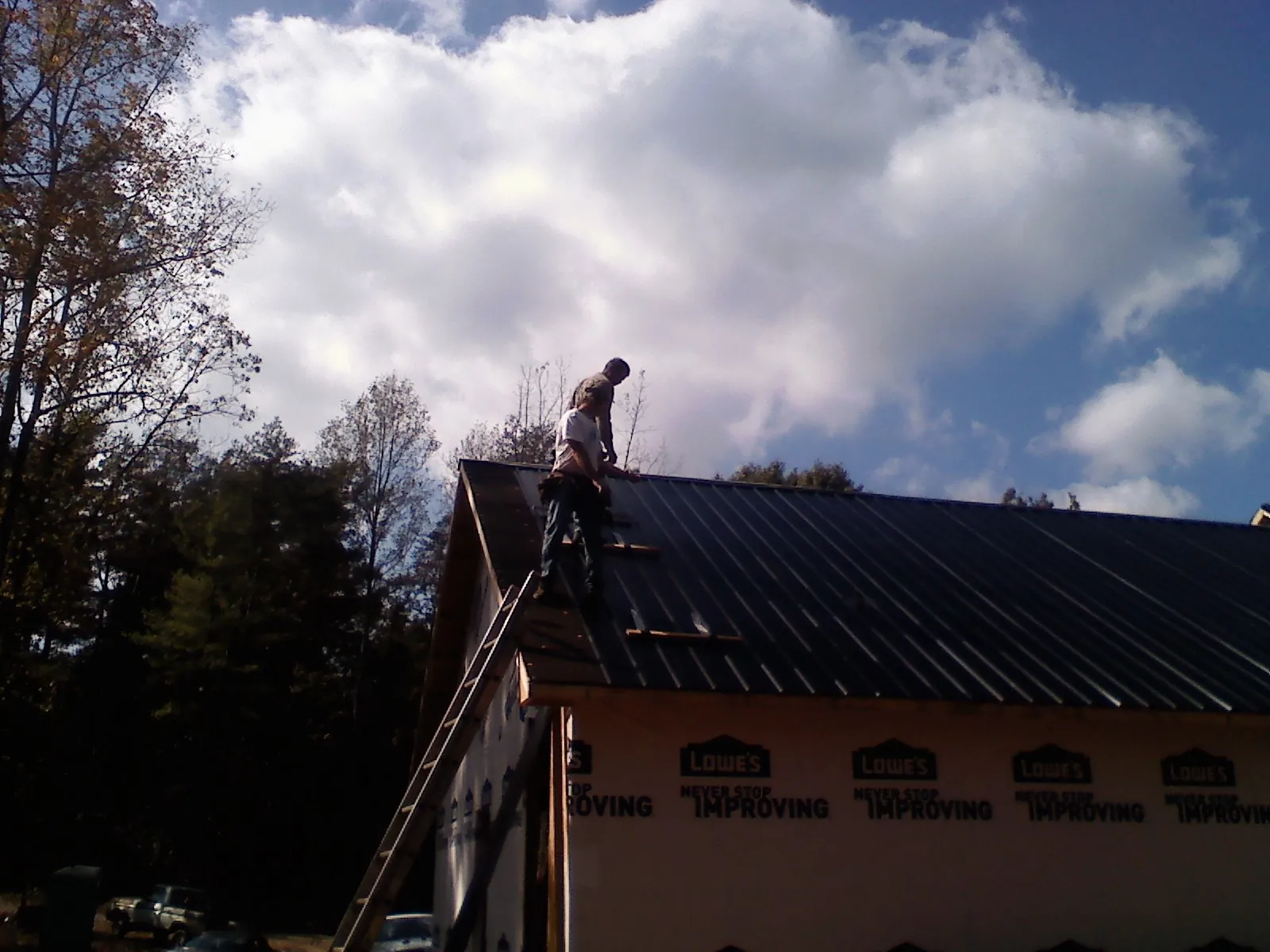 Roofer fastening dark metal panels high against a cloudy sky, from a Roof Inspection job in Nescopeck