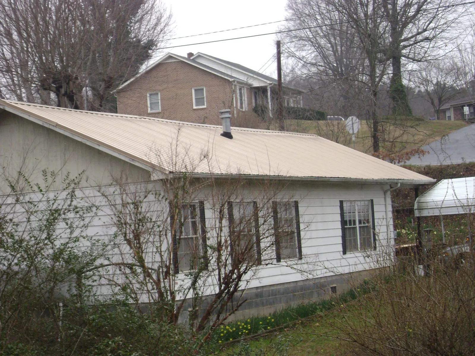 Tan metal roof on a white sided house set into a hillside — Commercial Roofing by Roofing Brothers in Nescopeck